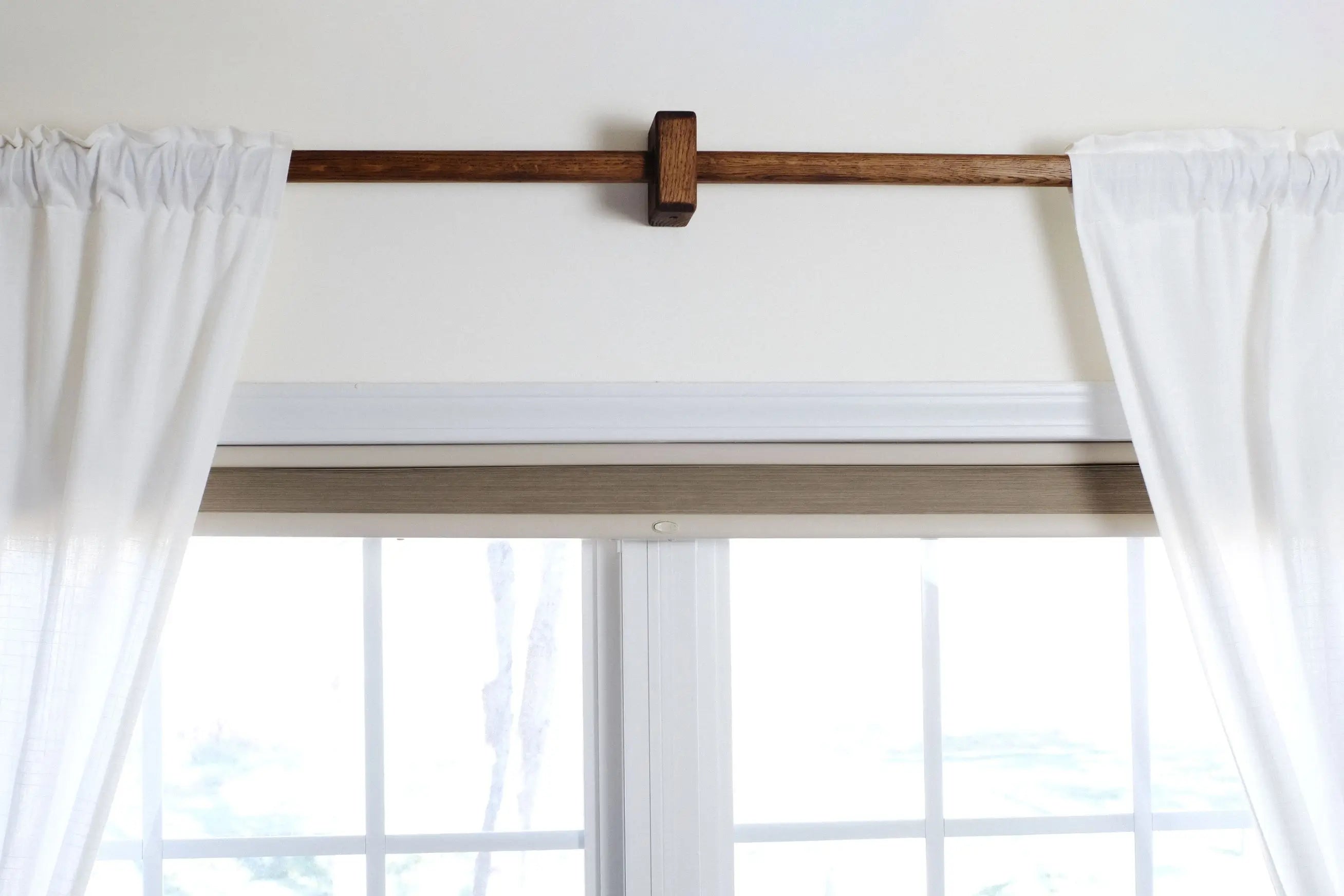 White curtains on a wooden curtain rod with a window in the background
