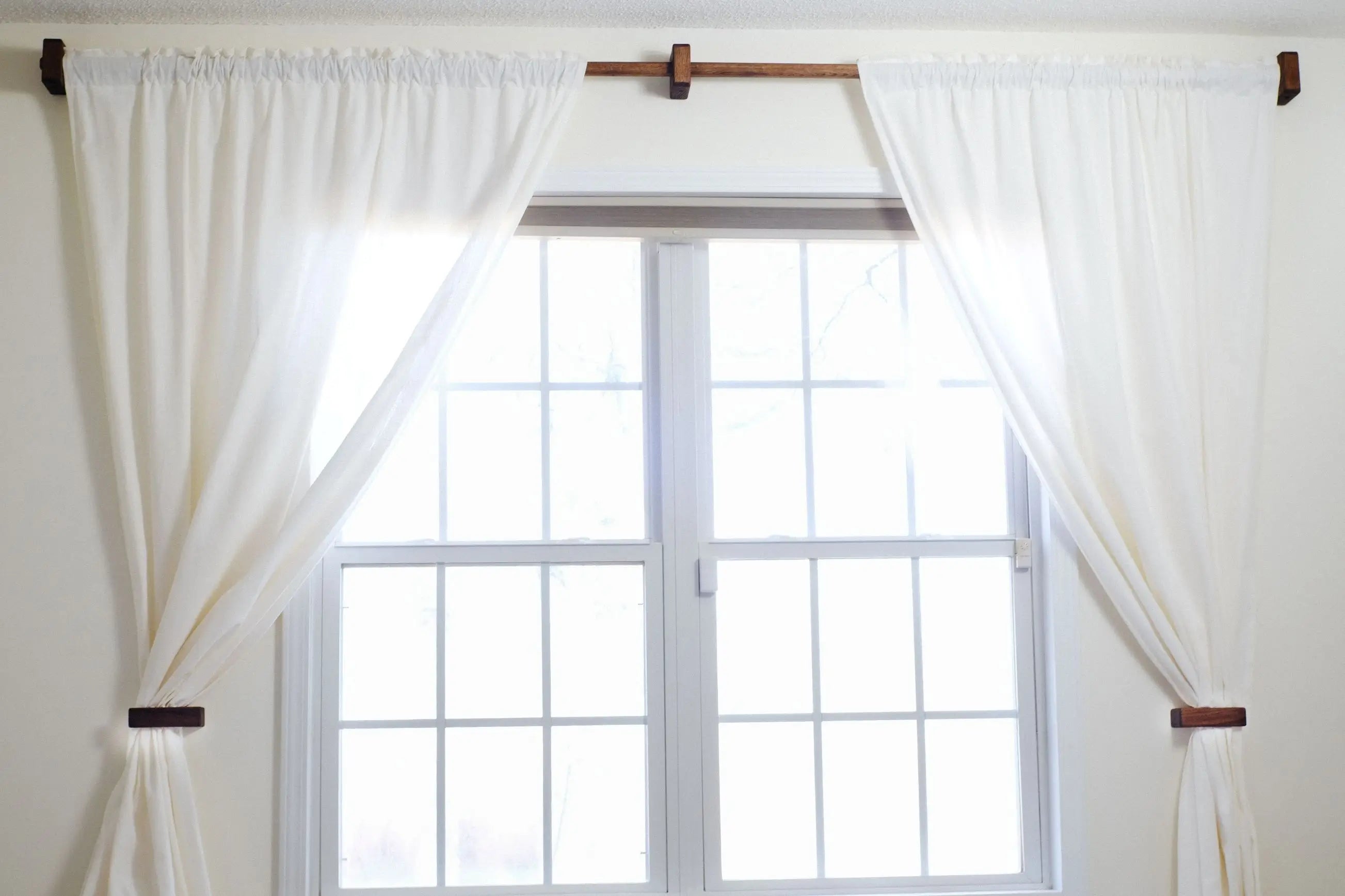 White curtains hanging on a window with wooden curtain rods.