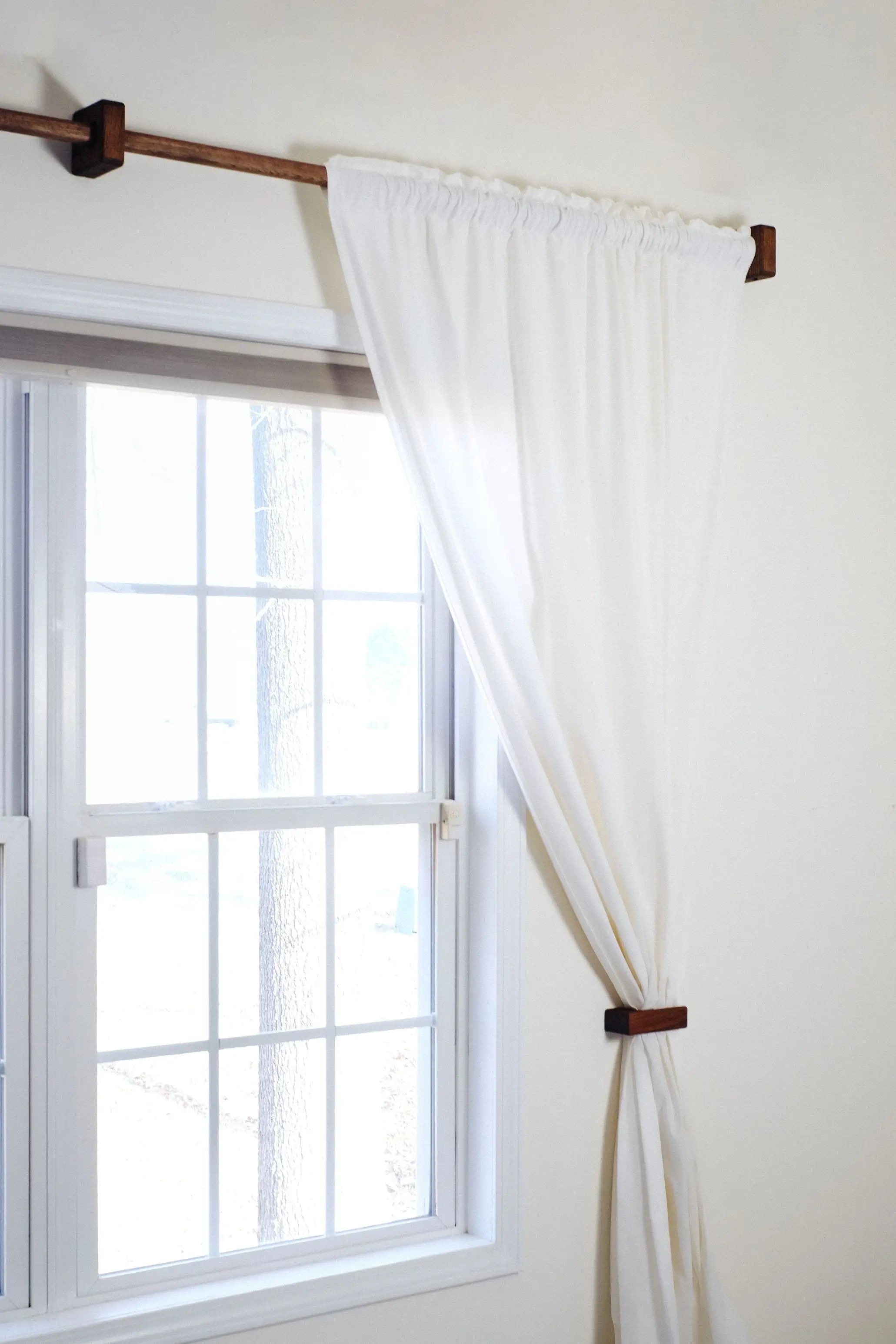 White curtain with wooden curtain rod on a window with white frame.