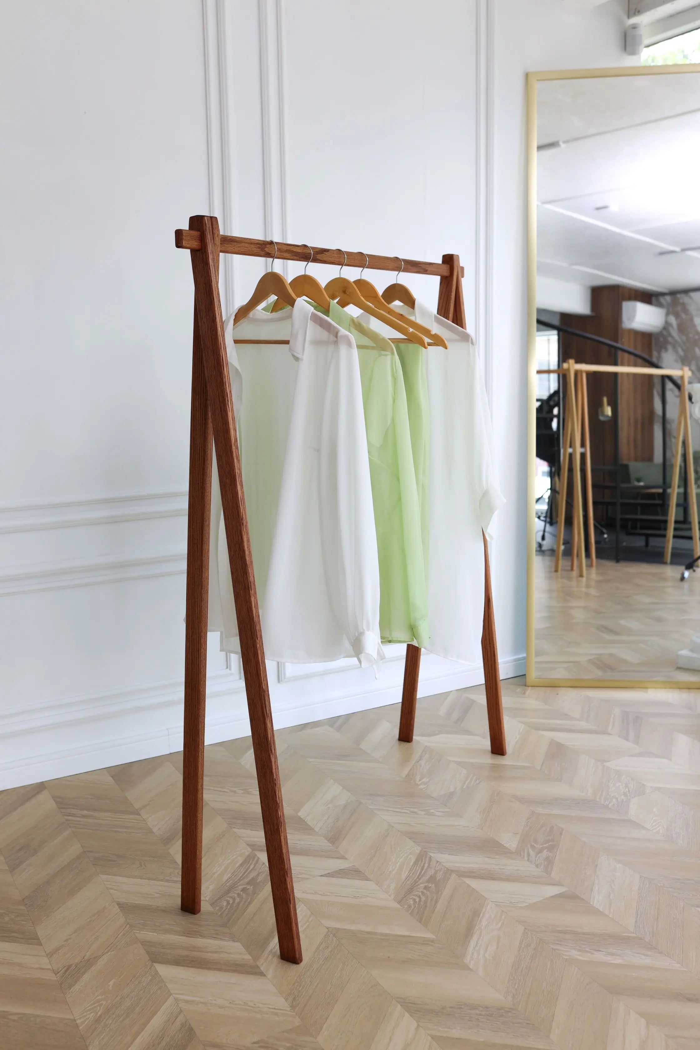 Wooden clothing rack with hangers holding white and green garments against a white wall.