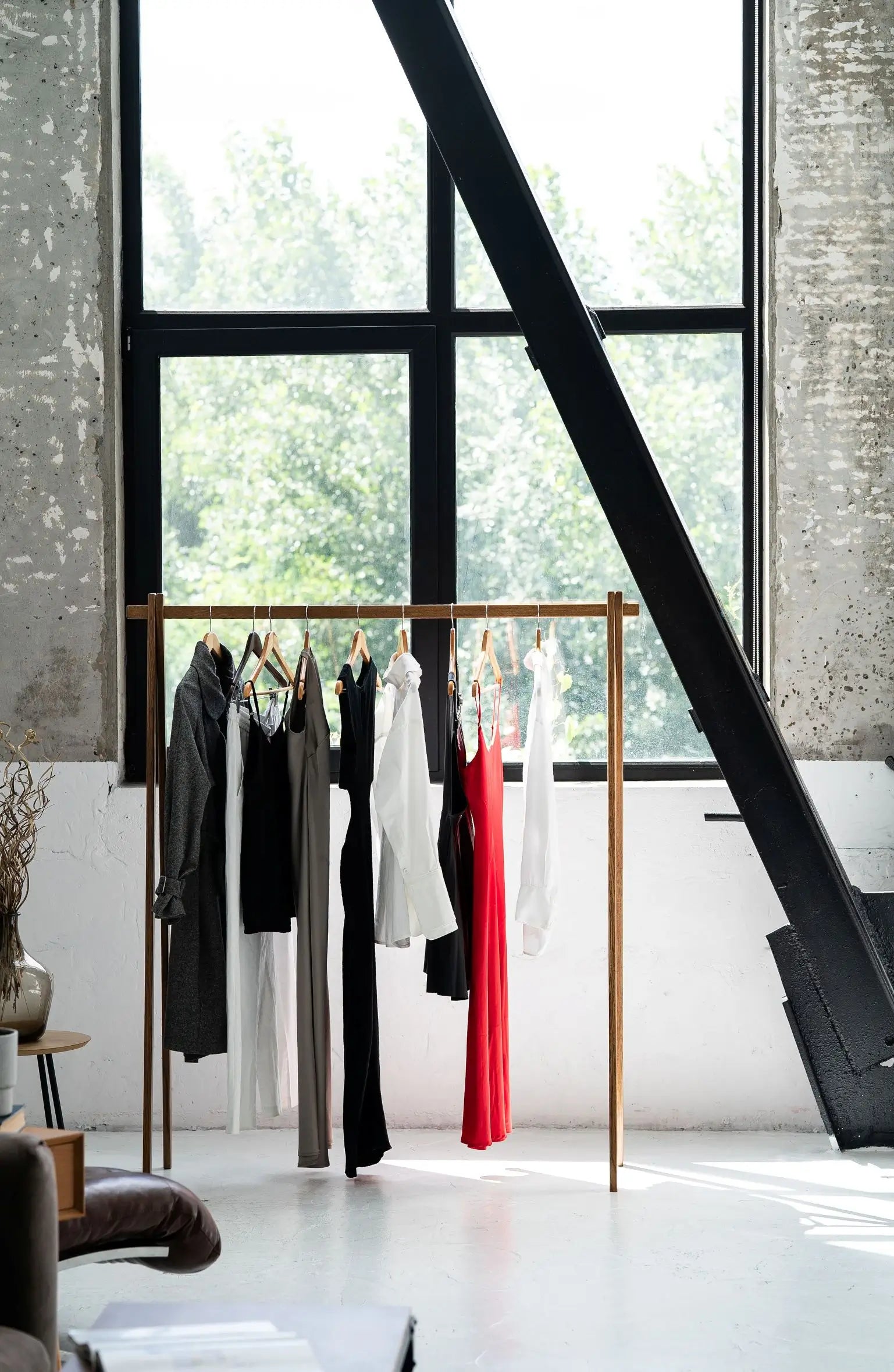 Clothing rack with clothes in a room with large windows and a staircase.