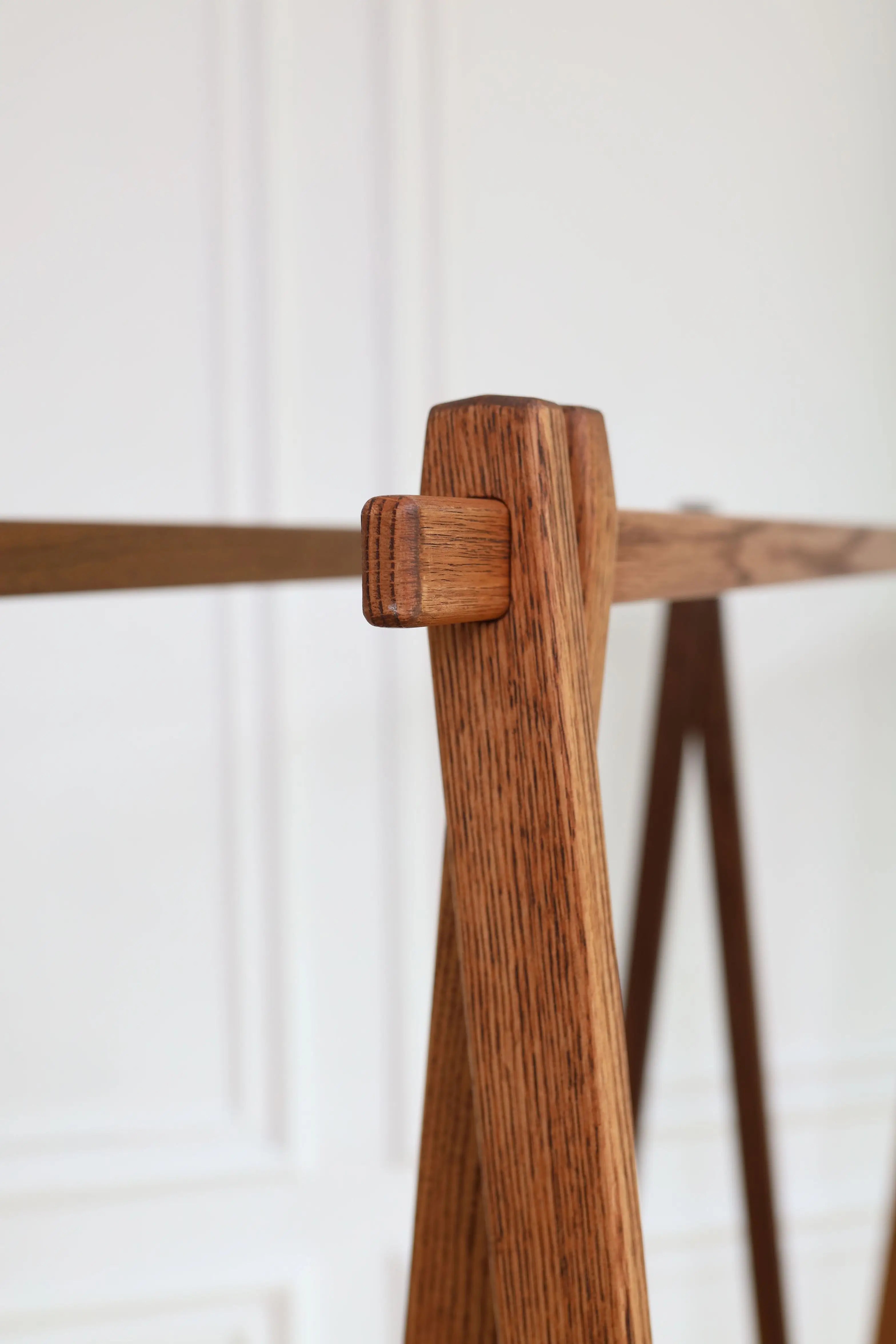 Wooden coat rack with a single wooden hook against a white wall.