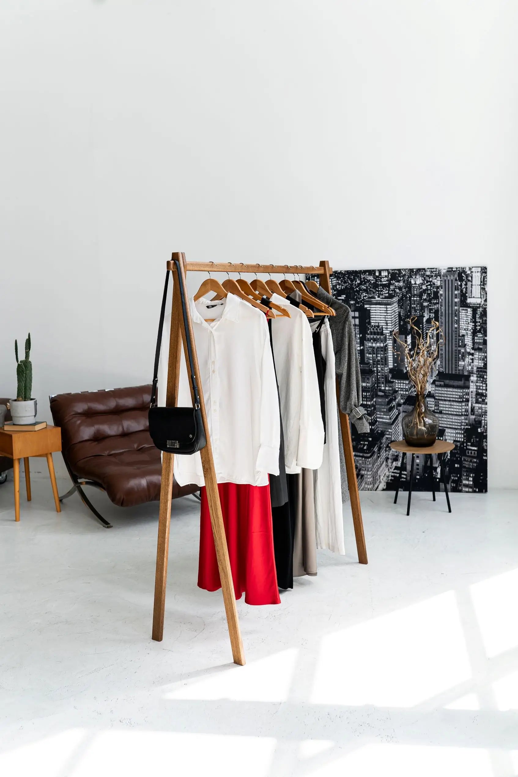 Wooden clothing rack with clothes in a minimalistic room with a cityscape painting.