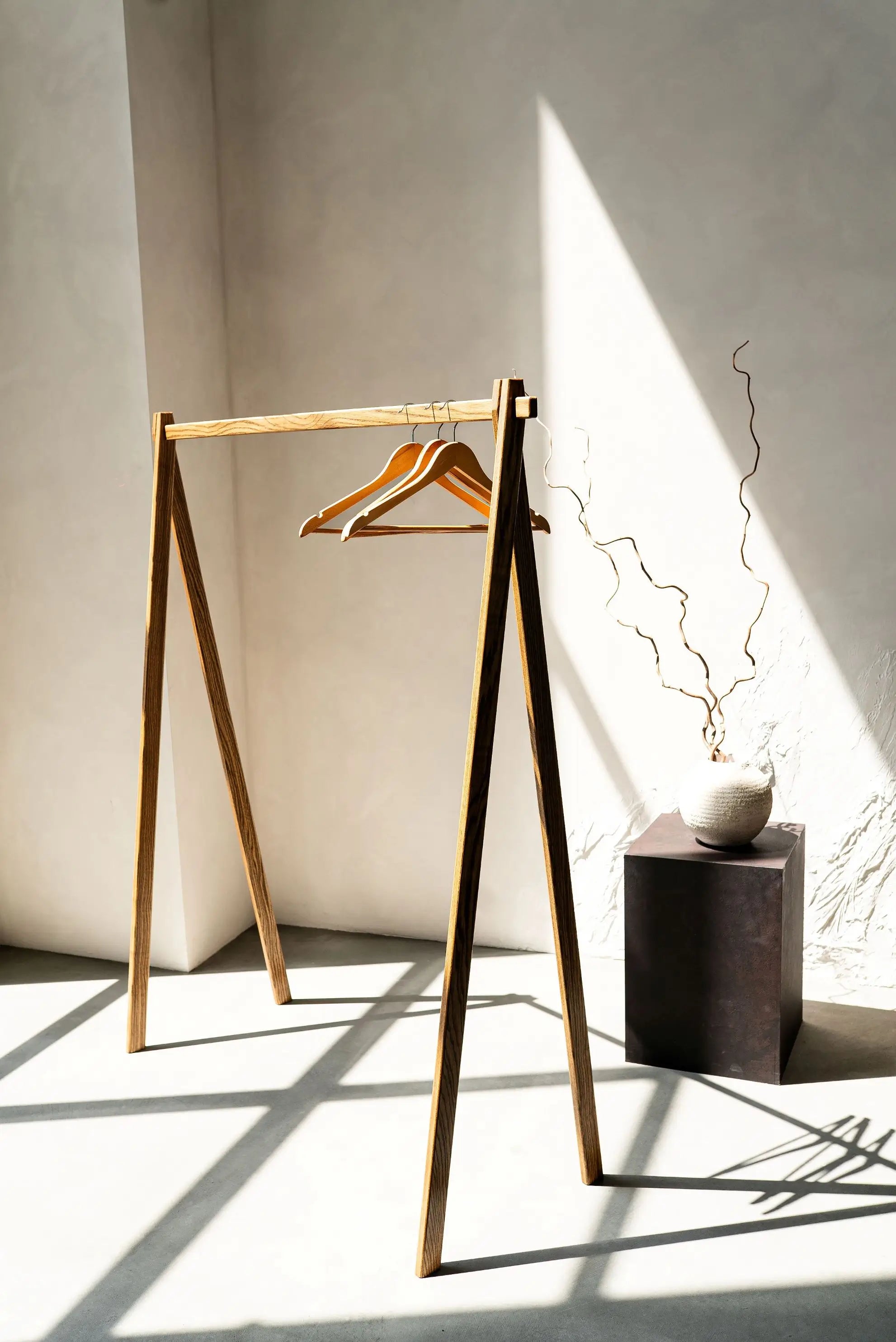 Wooden clothing rack with a hanger against a light wall with shadows.