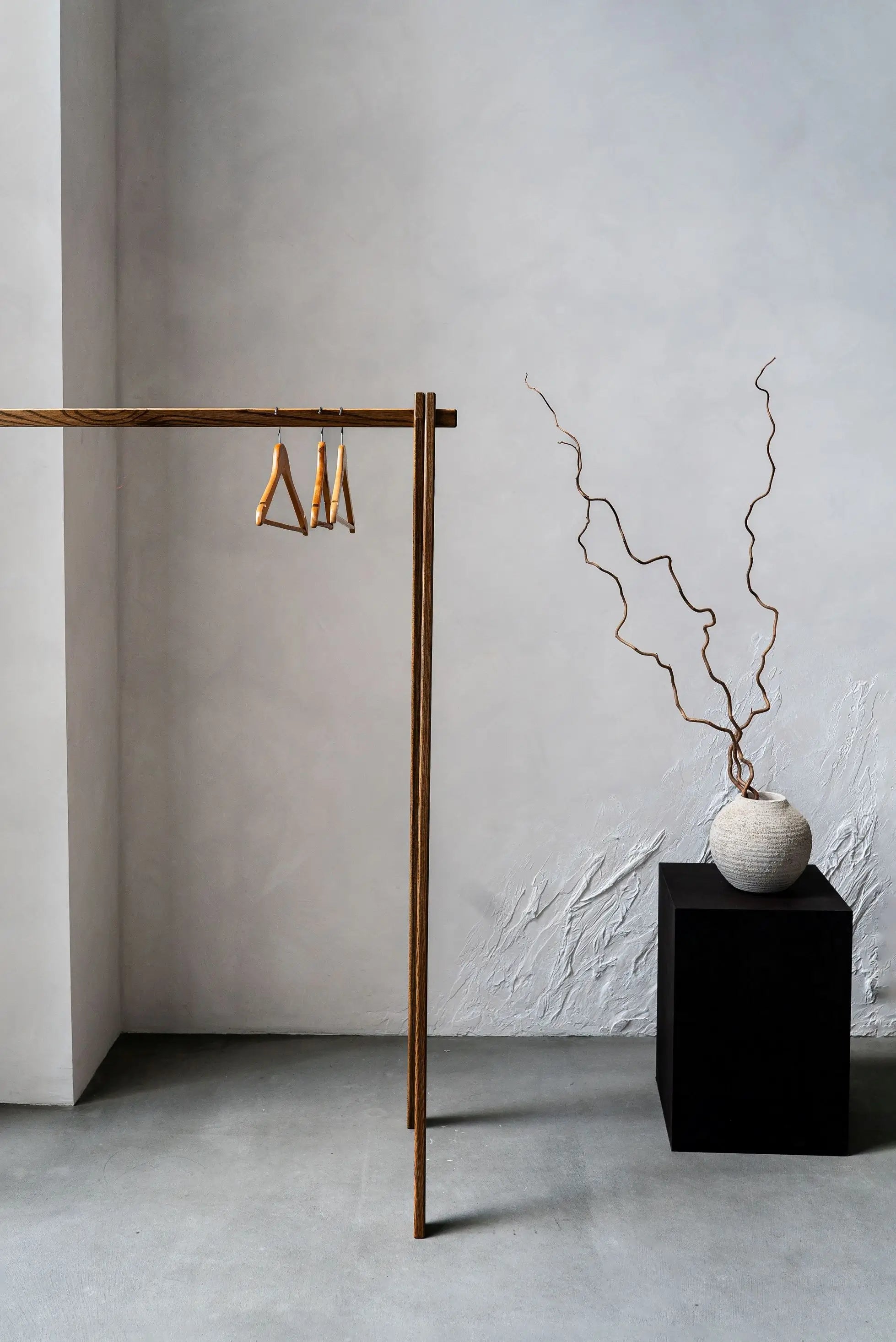 Gold earring stand with earrings against a white wall, next to a black cube with a vase and branches.