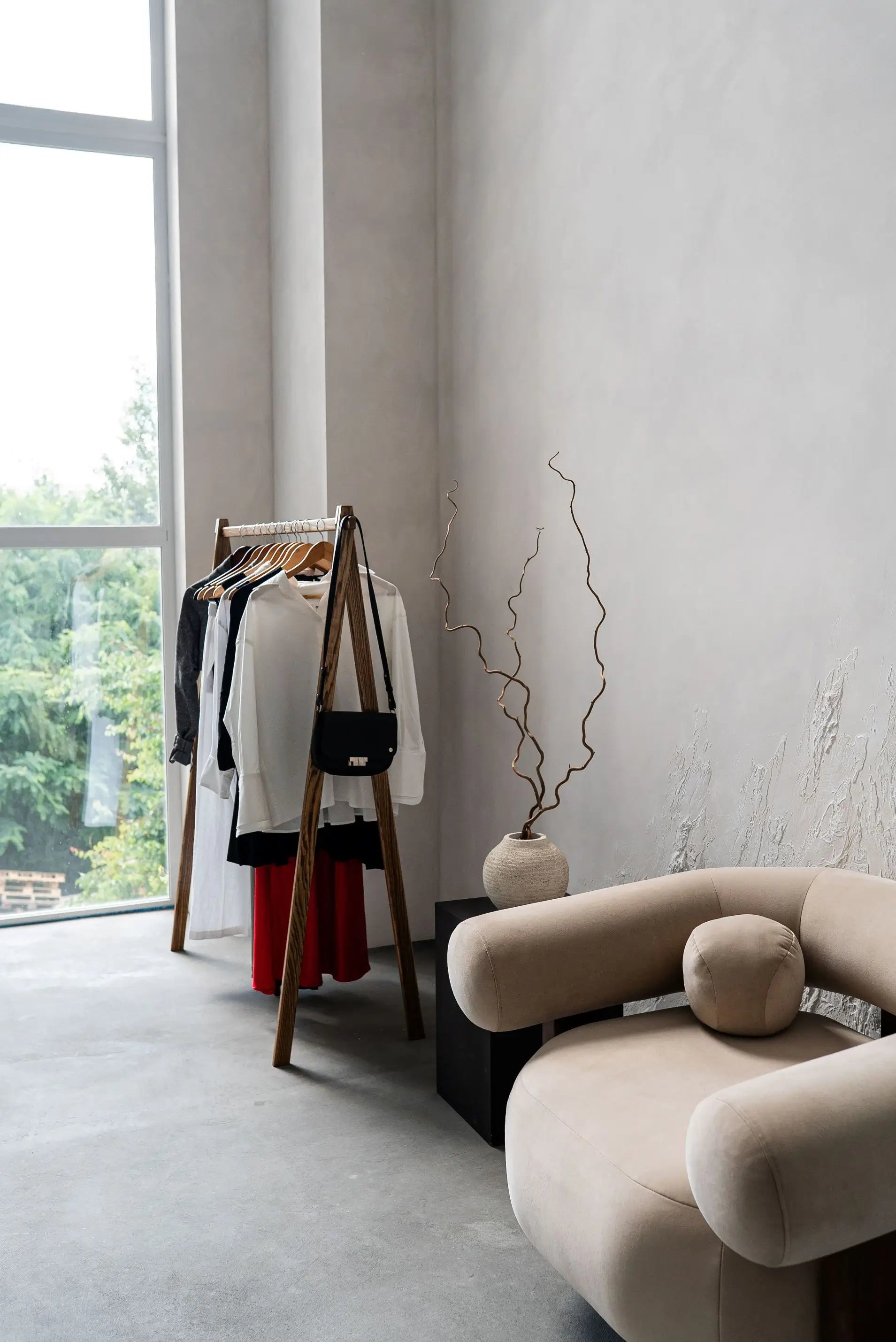 Modern living room with a beige sofa, clothing rack, and decorative plant.