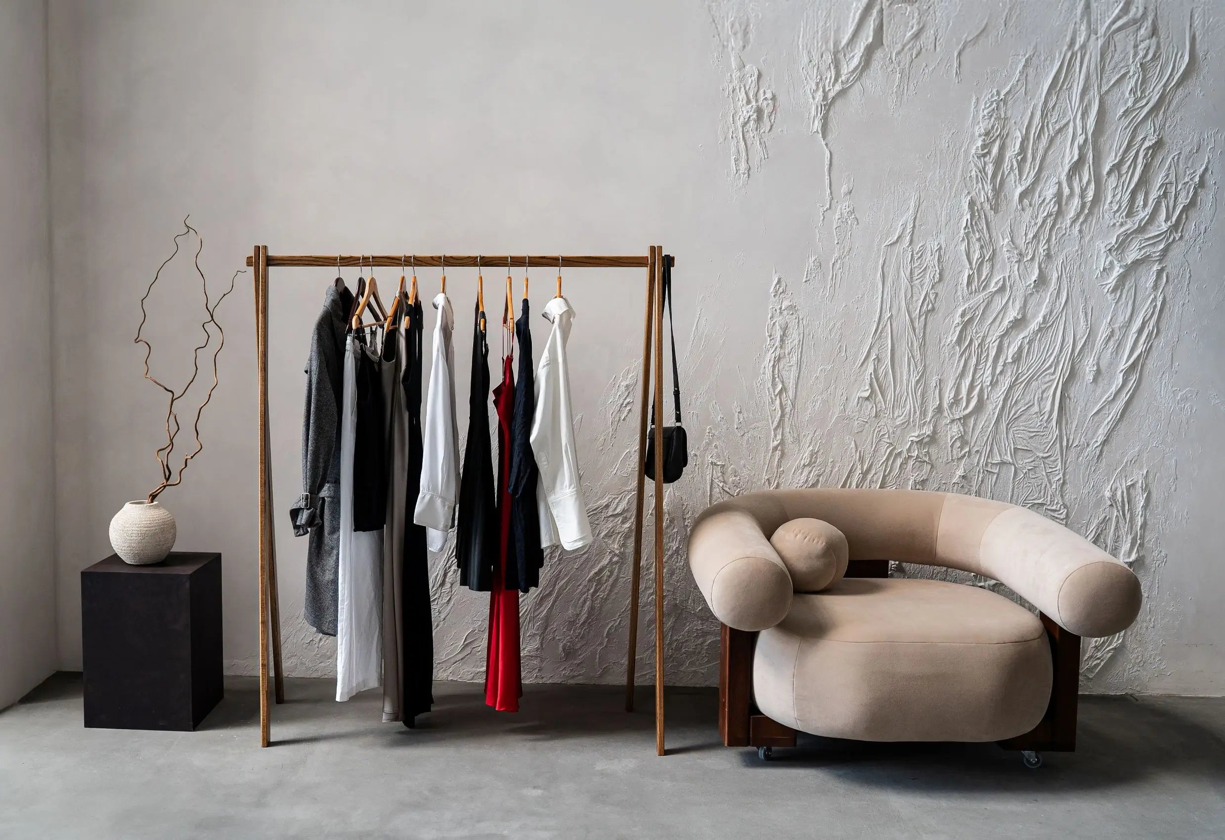 Clothing rack with clothes next to a modern chair against a textured wall.