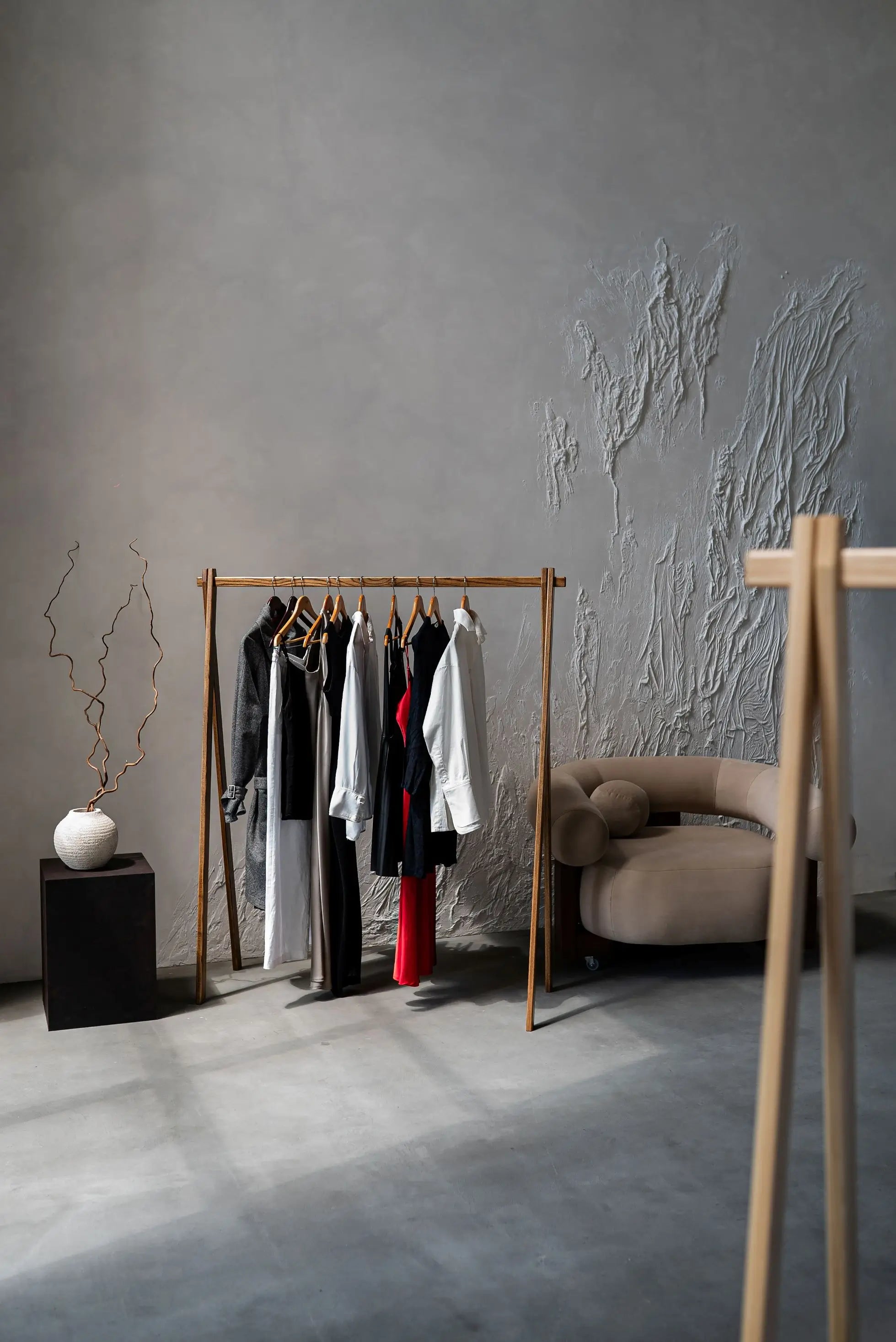Clothing rack with clothes against a textured gray wall in a minimalistic room.