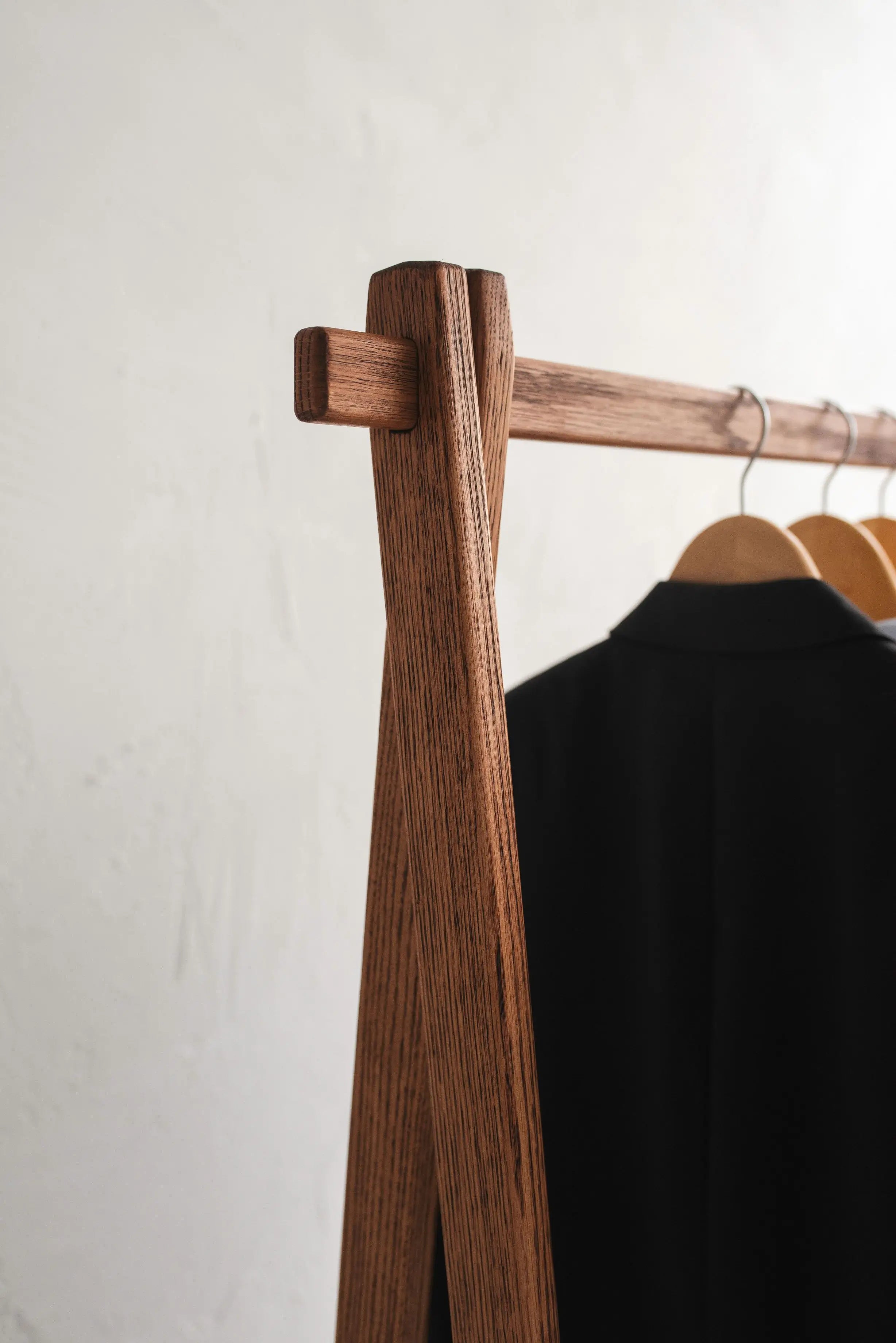 Wooden clothing rack with a black garment on a plain background