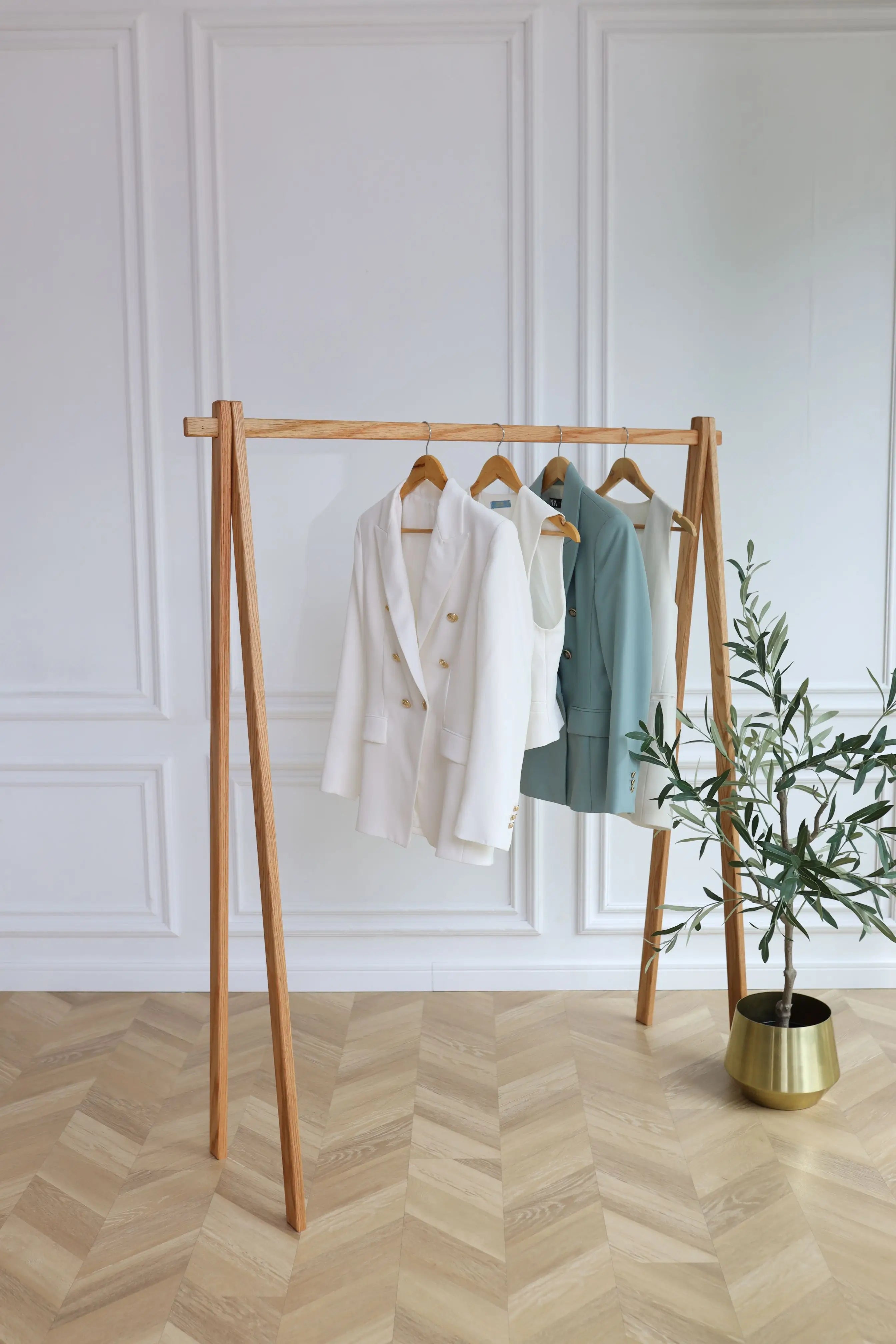 Wooden clothing rack with clothes against a white paneled wall.