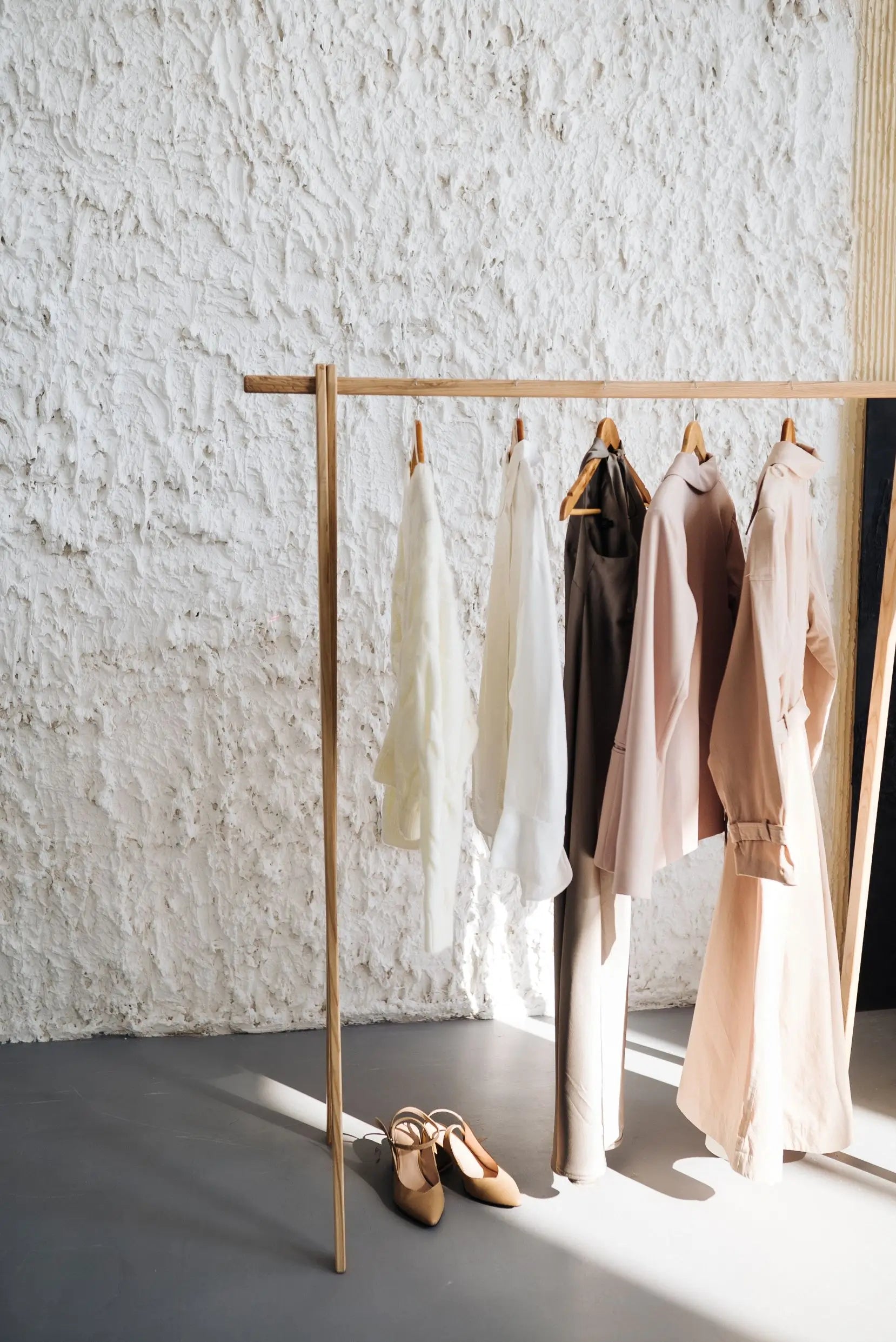 Clothing rack with various garments against a textured white wall.