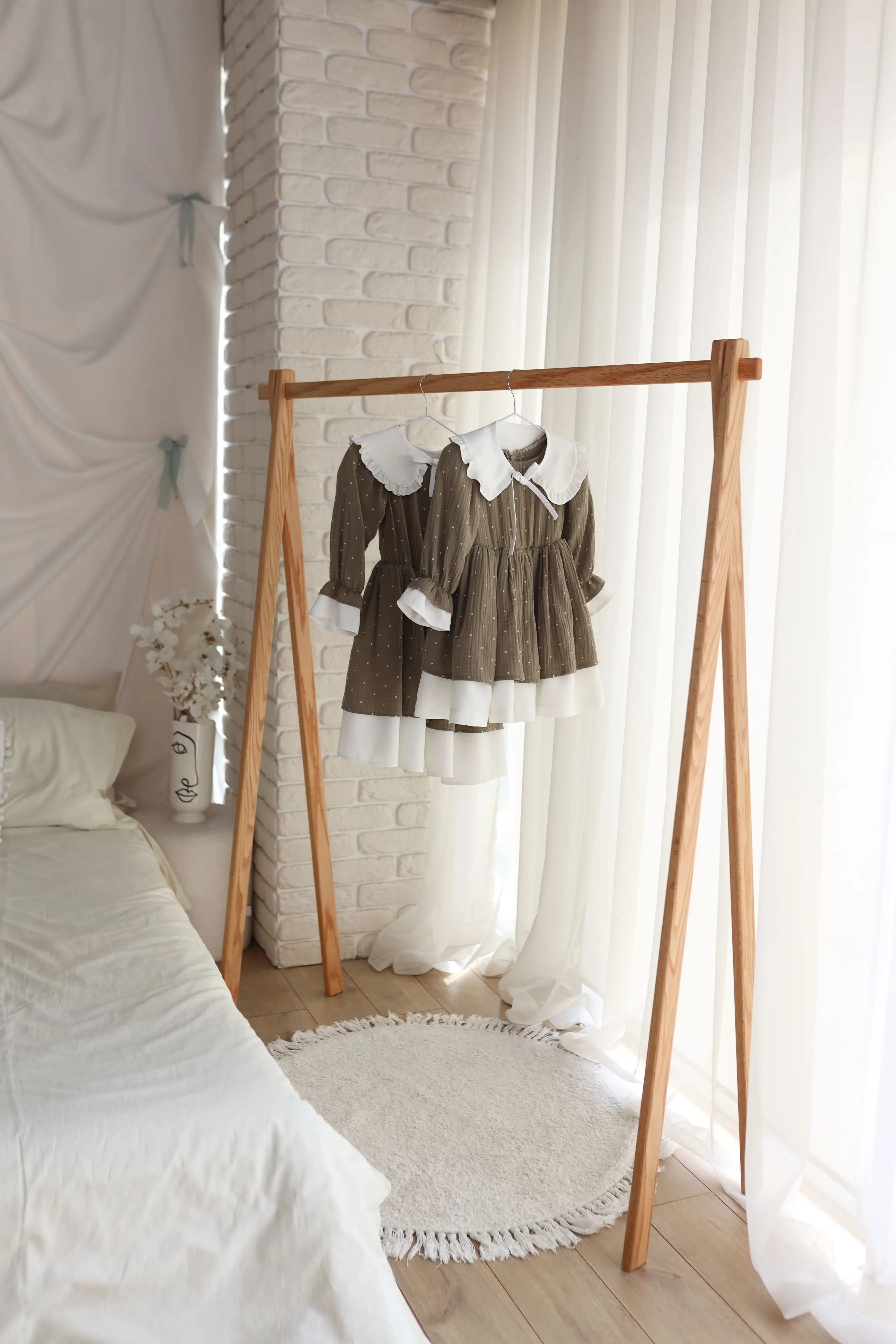 Children's dress on a wooden rack in a bedroom with white bedding and decor.