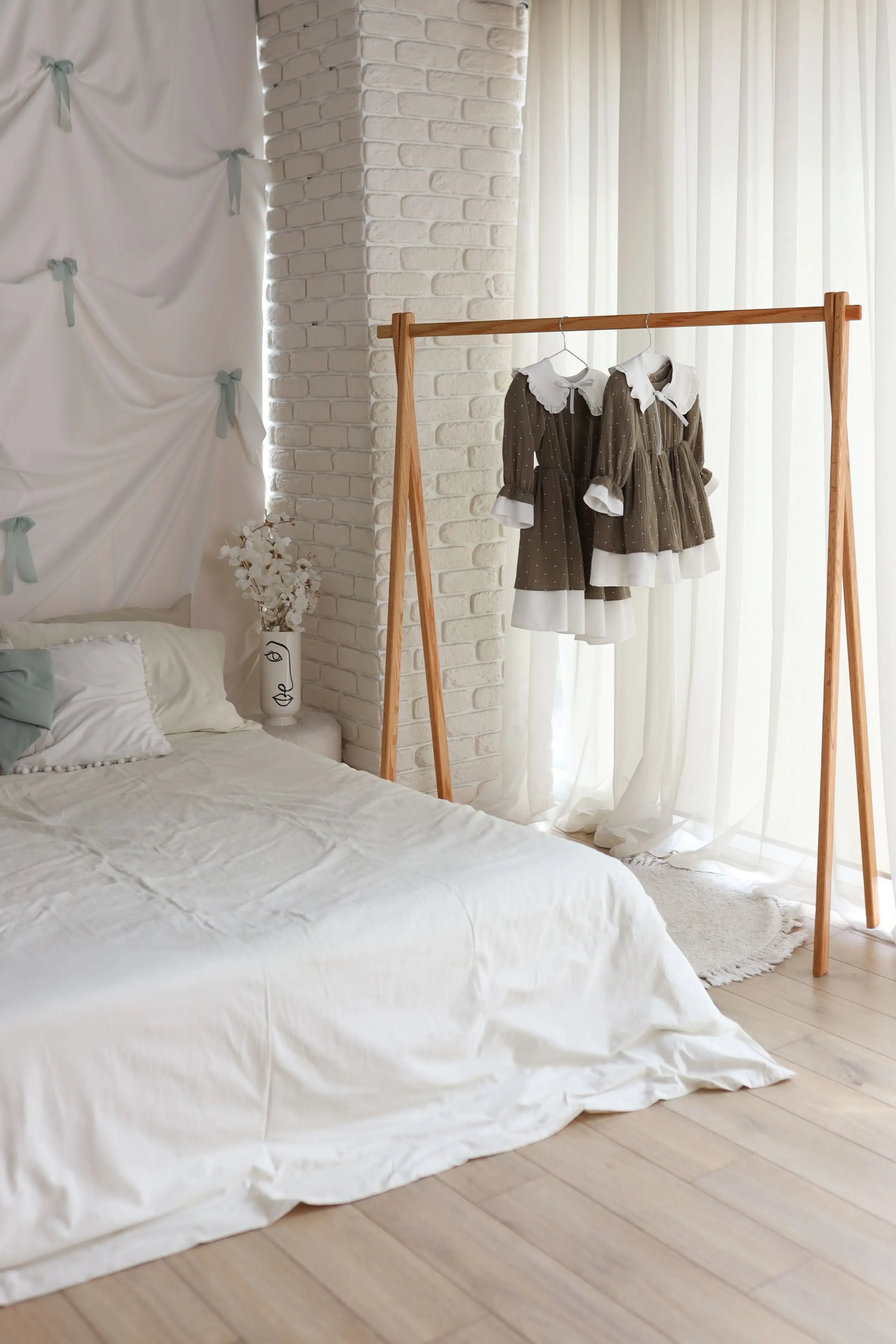 Bedroom with a bed, clothing rack, and white brick wall.