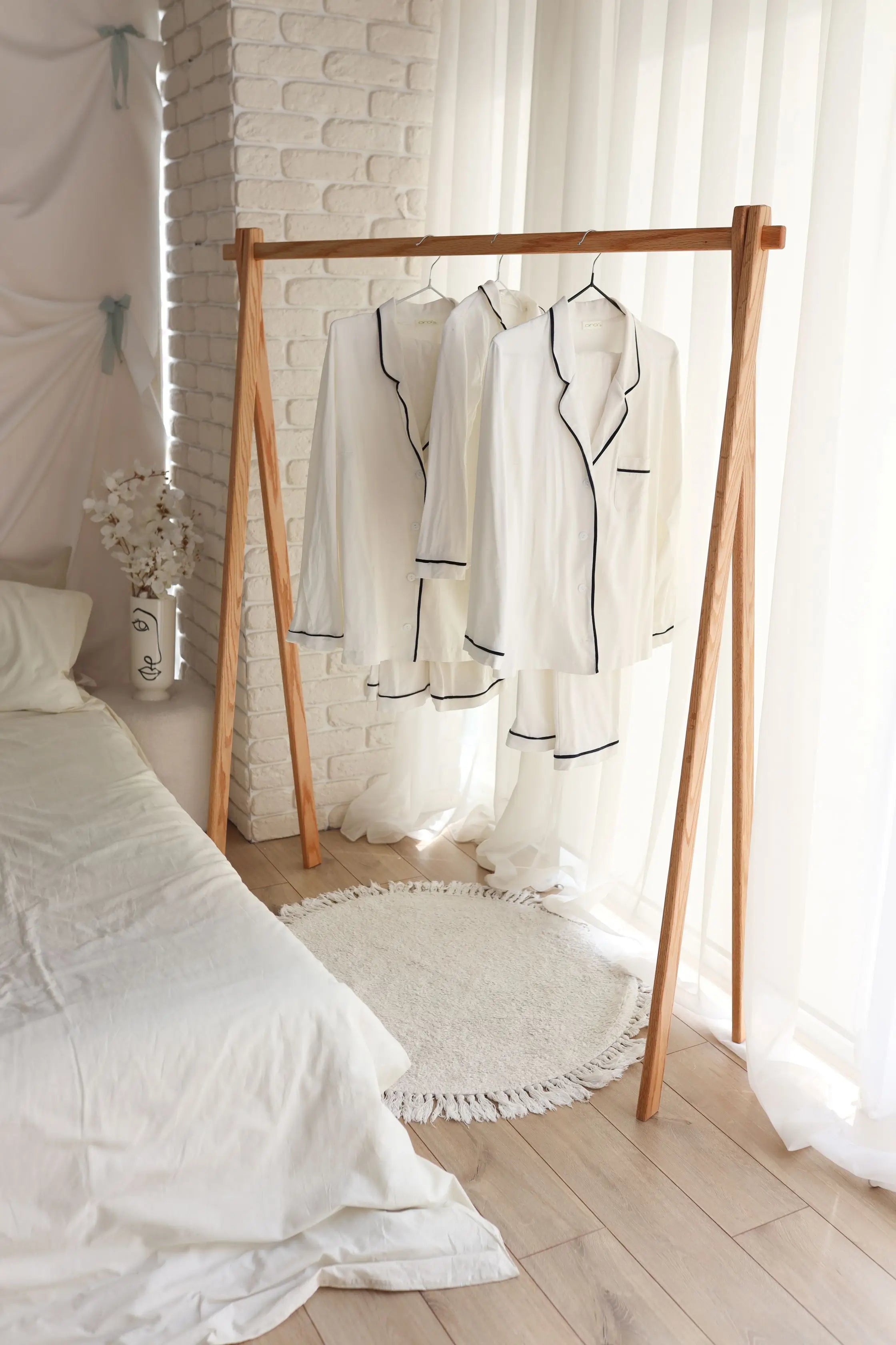 Wooden clothing rack with white garments against a white brick wall and light curtains.