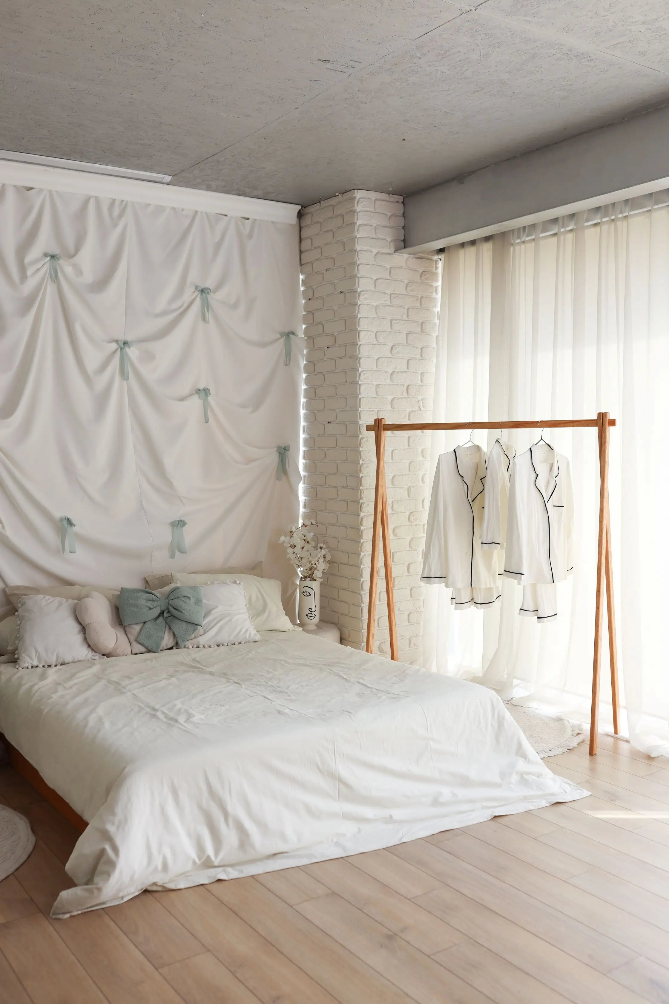 Modern bedroom with white bedding, wooden floor, and clothing rack.