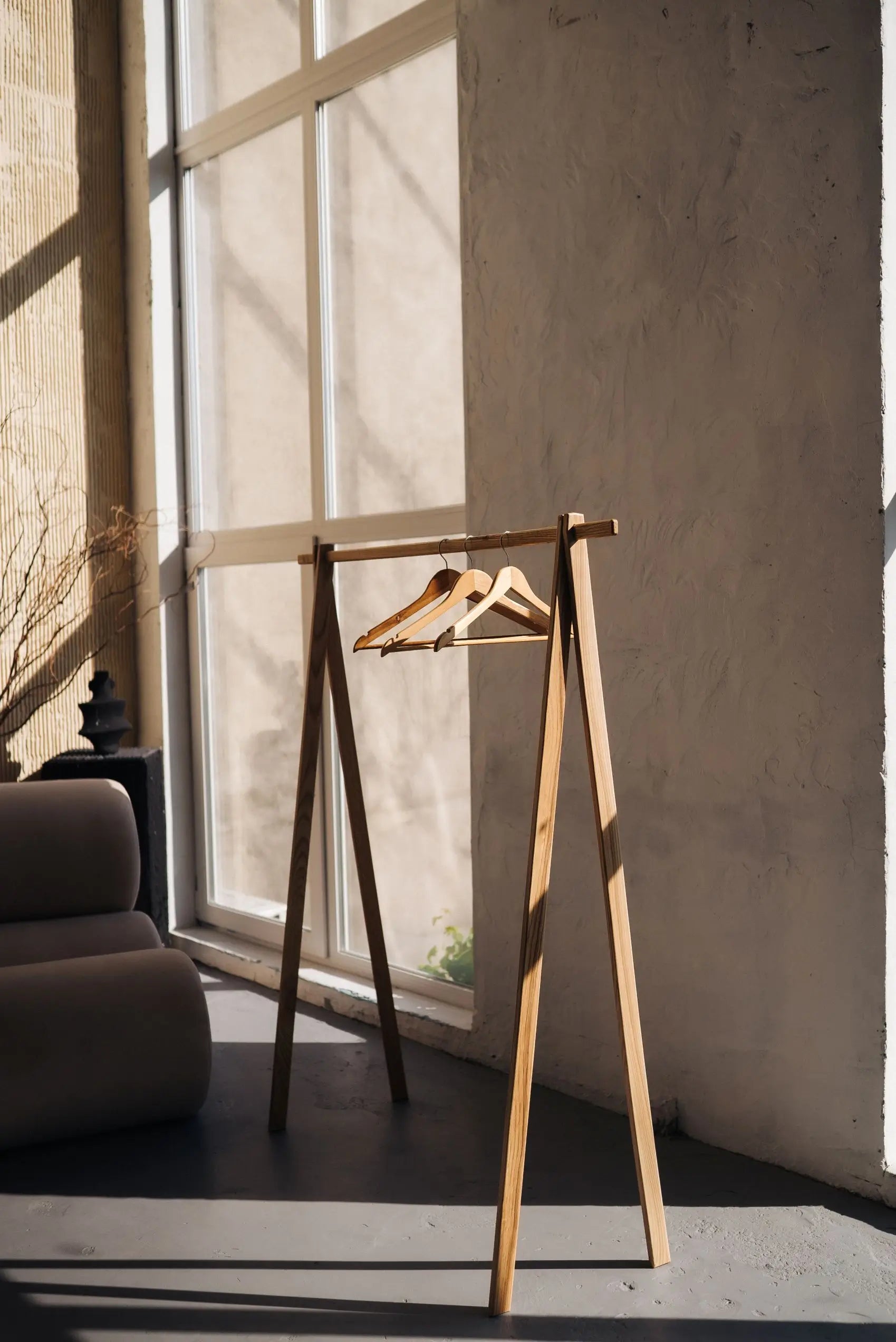Wooden hanger stand with a single wooden hanger against a neutral wall.