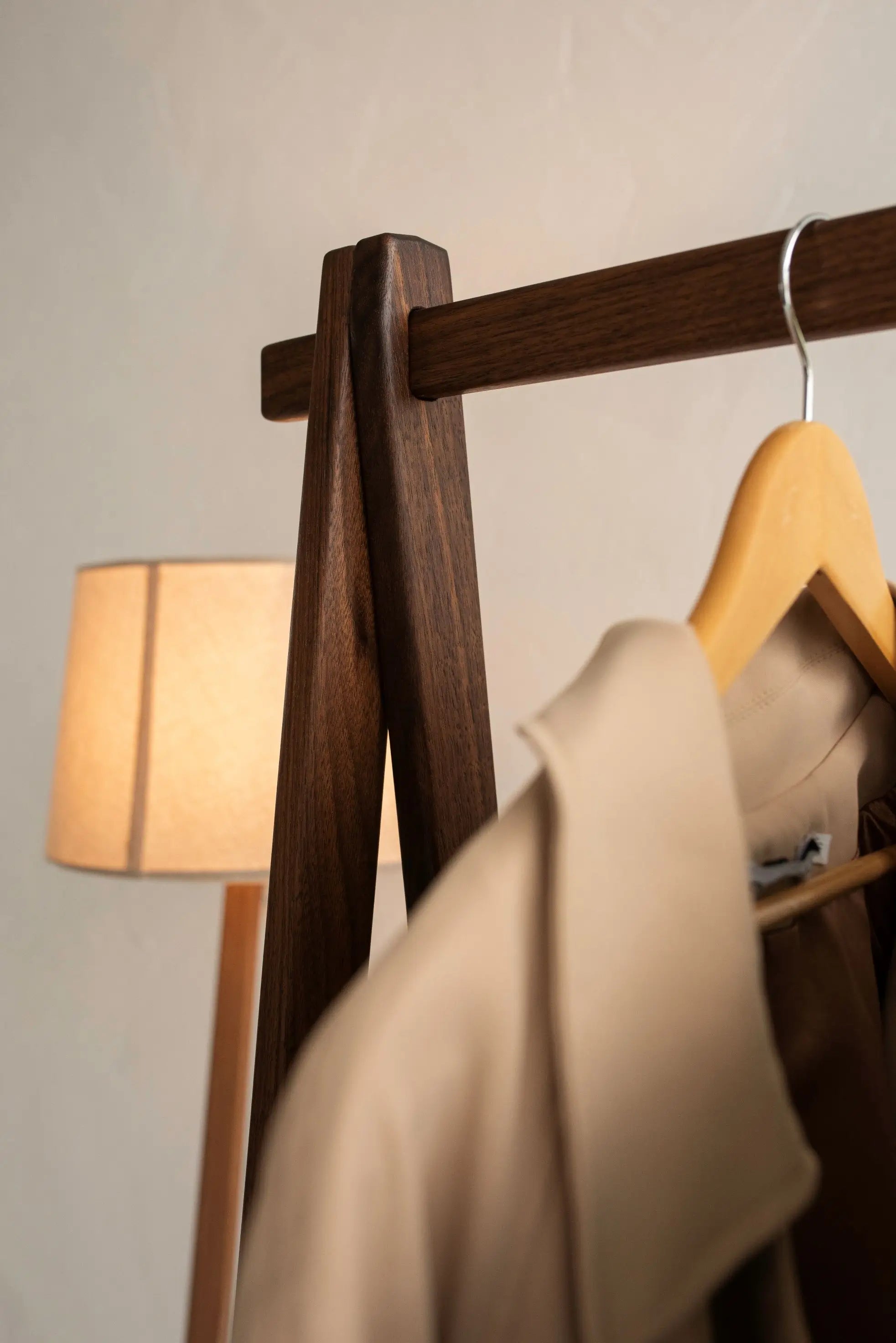 Hanger with beige garment on wooden rack against a neutral wall with a lamp.