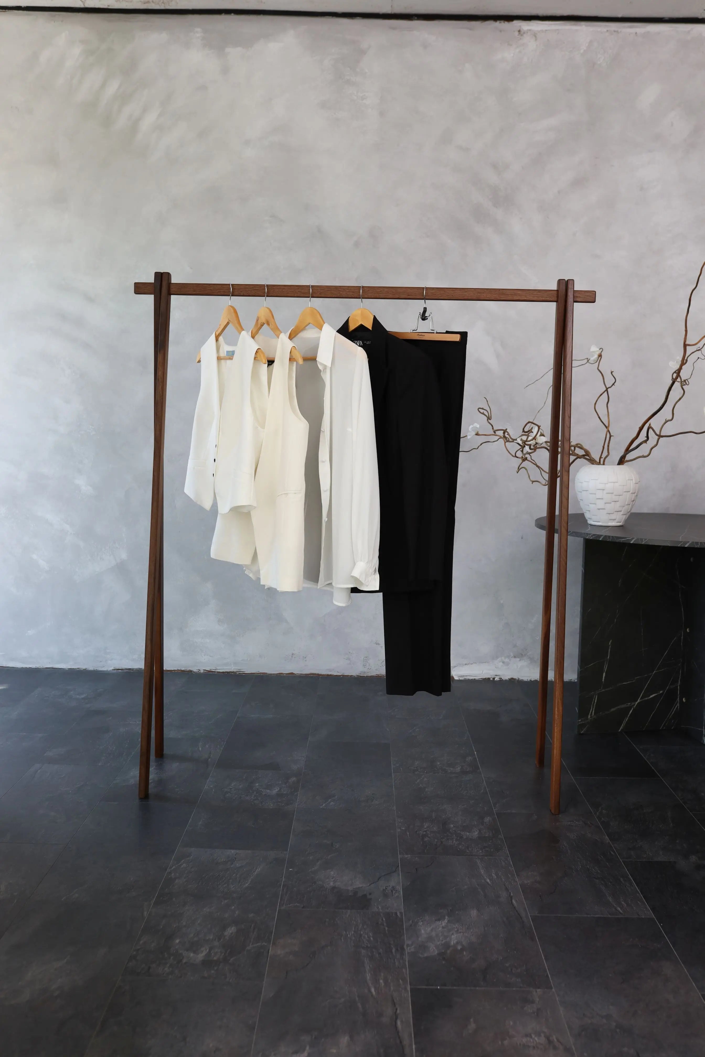 Wooden clothing rack with white and black garments against a gray wall.