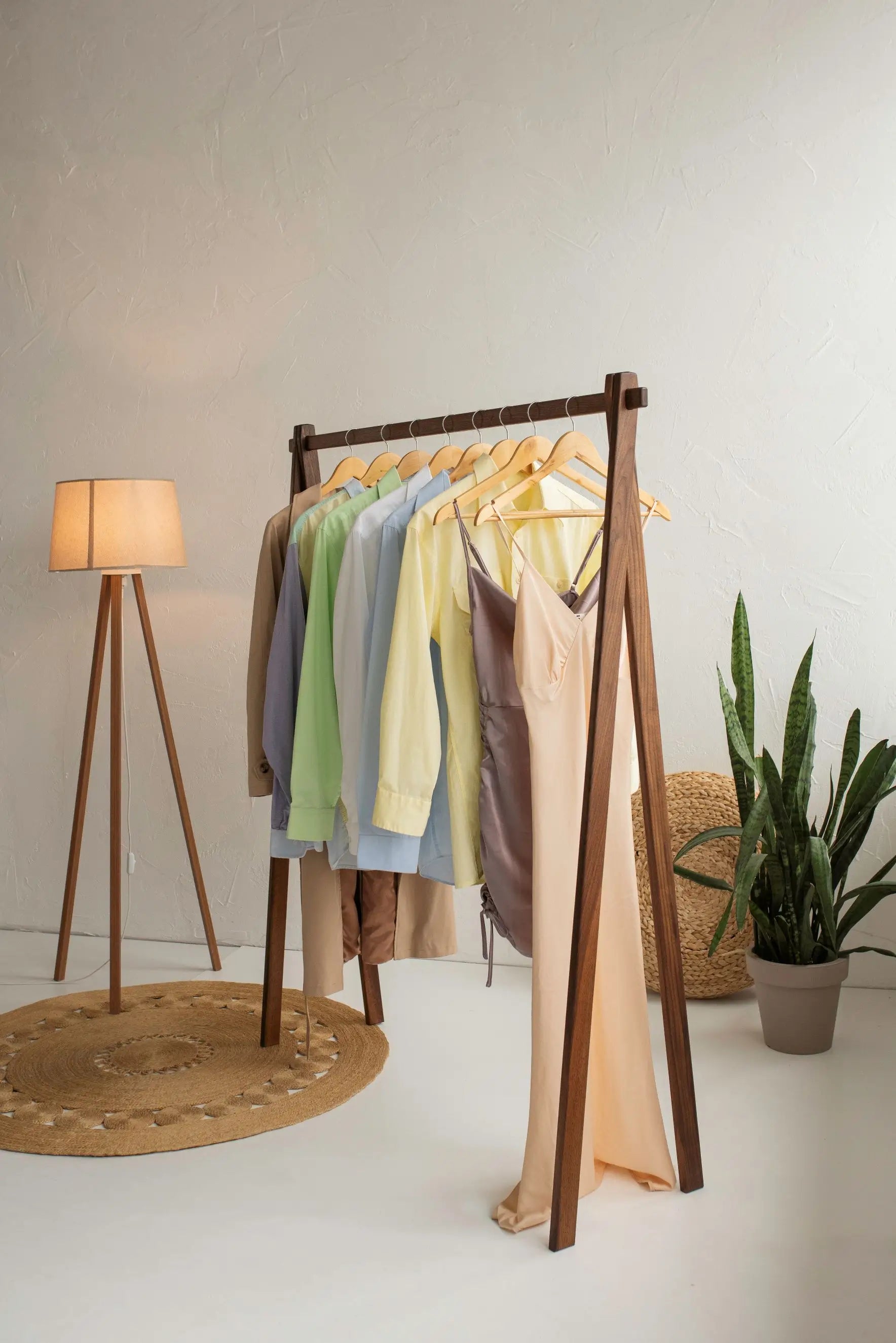 Wooden clothing rack with colorful shirts in a room with a lamp and plant.