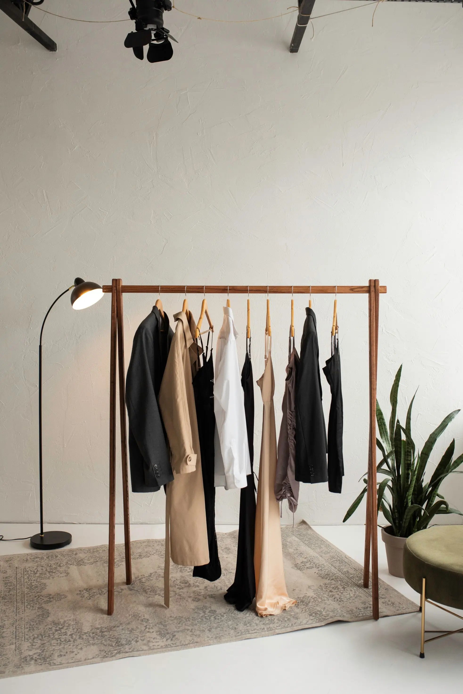 Clothing rack with clothes in a minimalistic room with a plant and lamp.