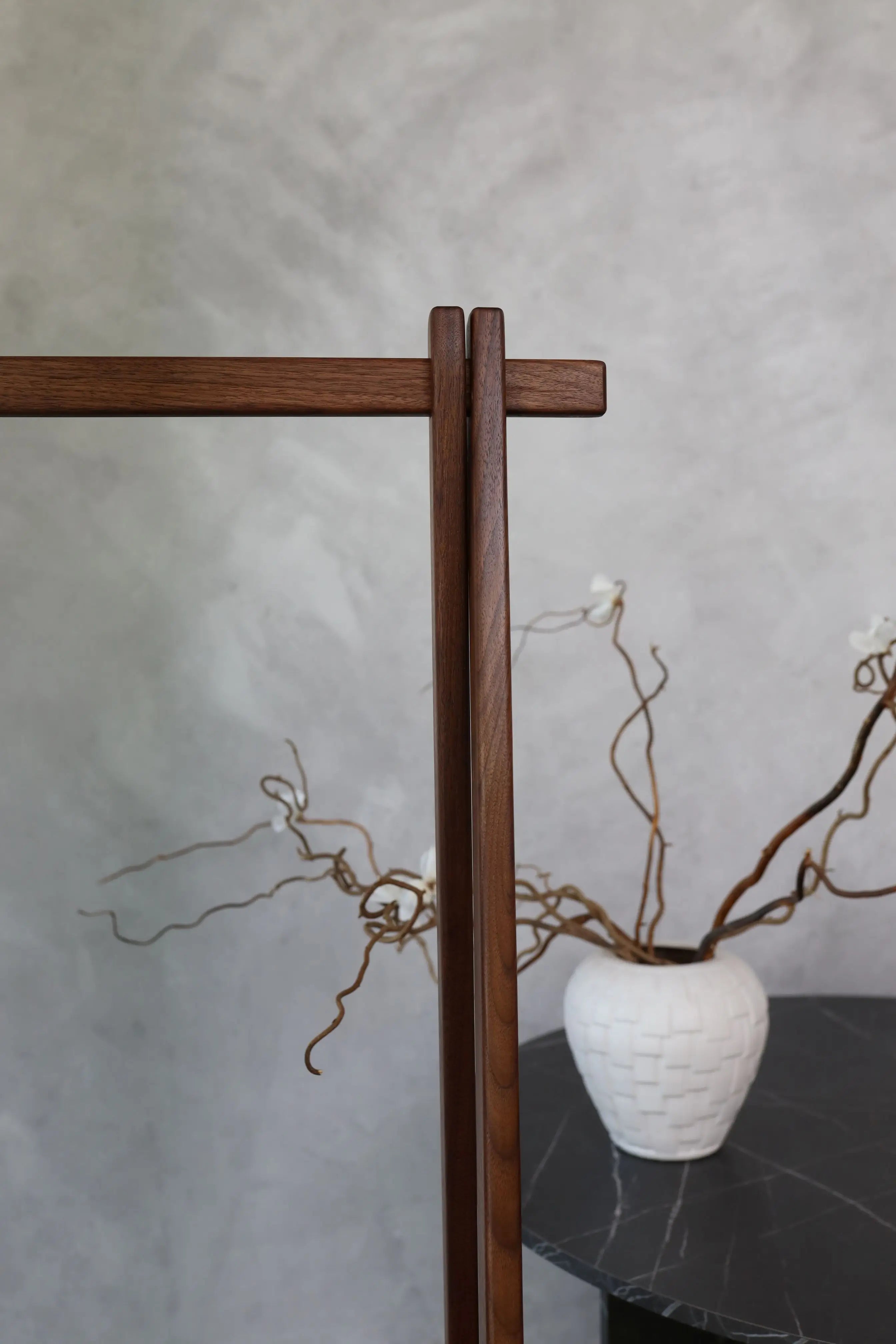 White vase with branches on a dark surface against a gray wall